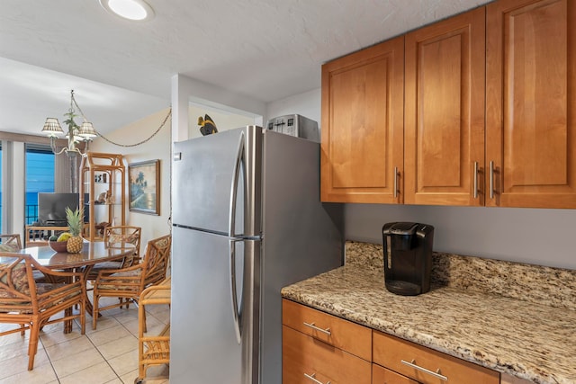 kitchen featuring a textured ceiling, stainless steel fridge, light tile patterned floors, a chandelier, and light stone counters