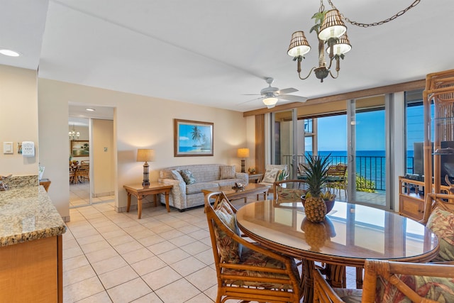 dining space with light tile patterned floors, a healthy amount of sunlight, ceiling fan with notable chandelier, and a water view