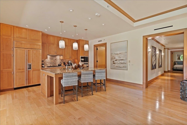 kitchen featuring pendant lighting, black appliances, a kitchen breakfast bar, a center island with sink, and light stone counters