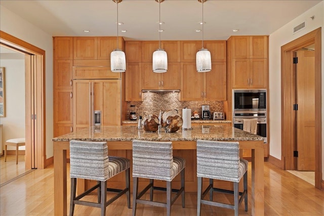 kitchen featuring decorative backsplash, built in appliances, light hardwood / wood-style flooring, and a kitchen island with sink