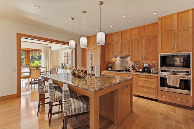 kitchen with stone counters, a center island with sink, oven, hanging light fixtures, and gas cooktop