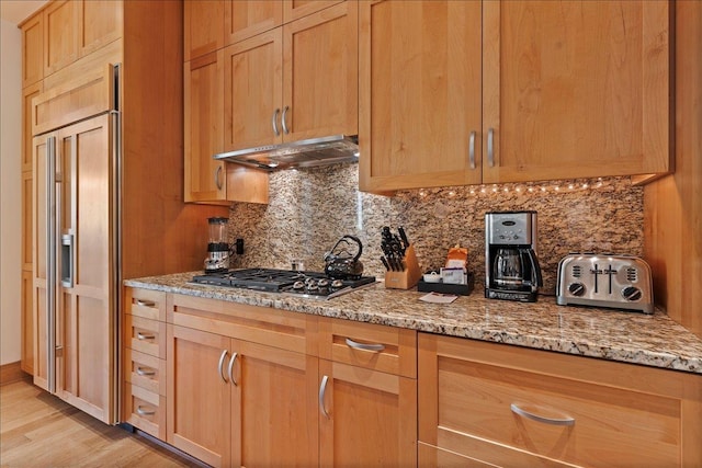 kitchen with light stone countertops, tasteful backsplash, light hardwood / wood-style flooring, paneled built in fridge, and stainless steel gas stovetop