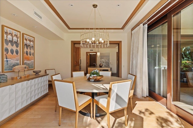 dining room featuring a raised ceiling, light hardwood / wood-style flooring, ornamental molding, and a notable chandelier