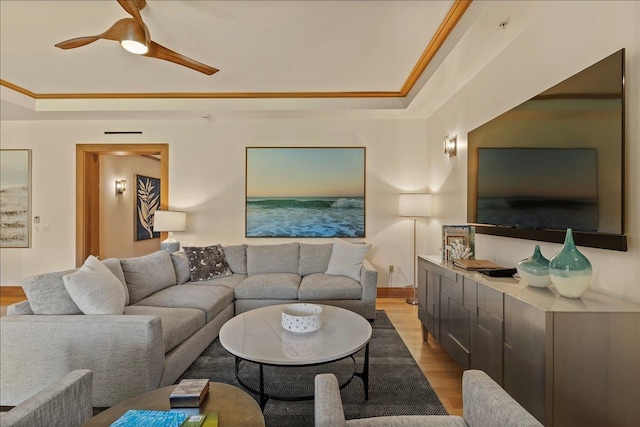 living room with a raised ceiling, crown molding, ceiling fan, and light hardwood / wood-style floors