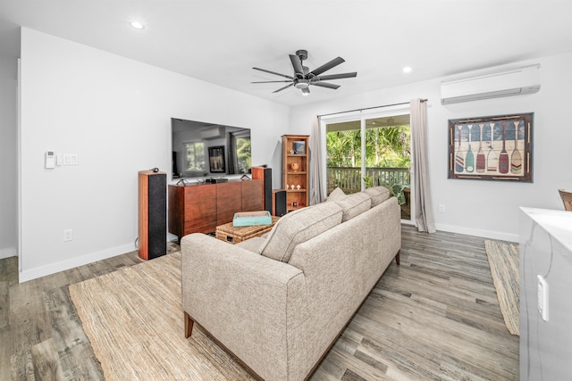 living room featuring a wall unit AC, light hardwood / wood-style floors, and ceiling fan