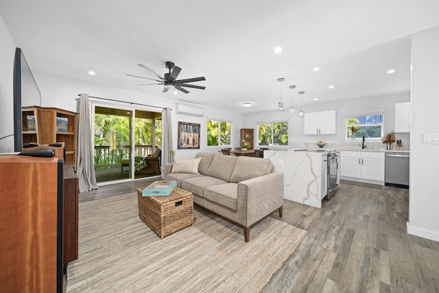 living room featuring ceiling fan, sink, a wall unit AC, and light hardwood / wood-style floors