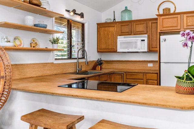 kitchen featuring wooden counters, a kitchen breakfast bar, white appliances, vaulted ceiling, and sink