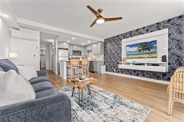 living room featuring light hardwood / wood-style floors, ceiling fan, a wall mounted air conditioner, and sink