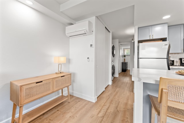 kitchen with white refrigerator, gray cabinets, stacked washing maching and dryer, a wall mounted air conditioner, and light wood-type flooring