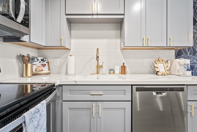 kitchen featuring tasteful backsplash, gray cabinetry, stainless steel appliances, and sink