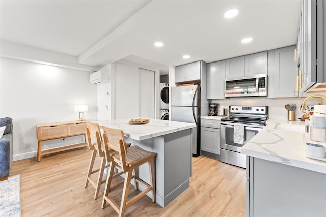 kitchen with light hardwood / wood-style floors, stacked washer / drying machine, gray cabinetry, and stainless steel appliances