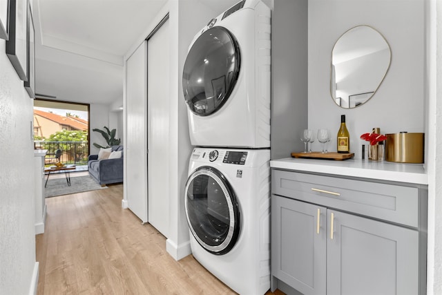 clothes washing area featuring stacked washer and clothes dryer, cabinets, and light wood-type flooring