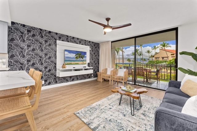 living room featuring wood-type flooring, ceiling fan, and a wall of windows