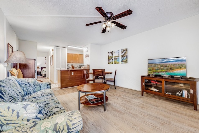 living room with ceiling fan, a textured ceiling, and light hardwood / wood-style floors