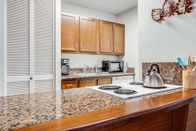 kitchen with light stone counters, sink, and white cooktop