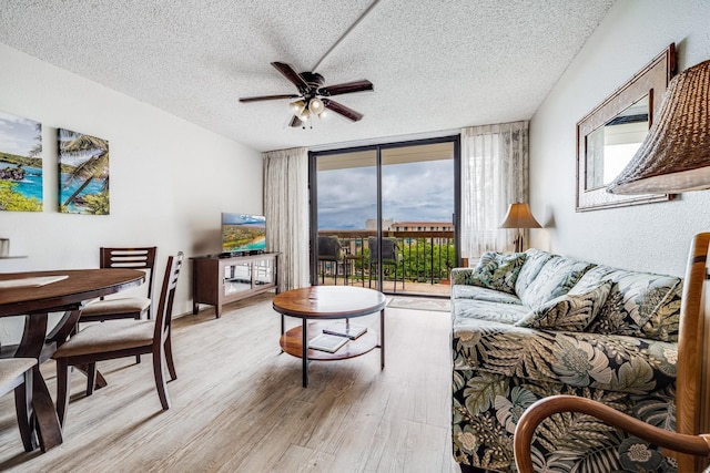 living room featuring ceiling fan, a wall of windows, light hardwood / wood-style floors, and a textured ceiling