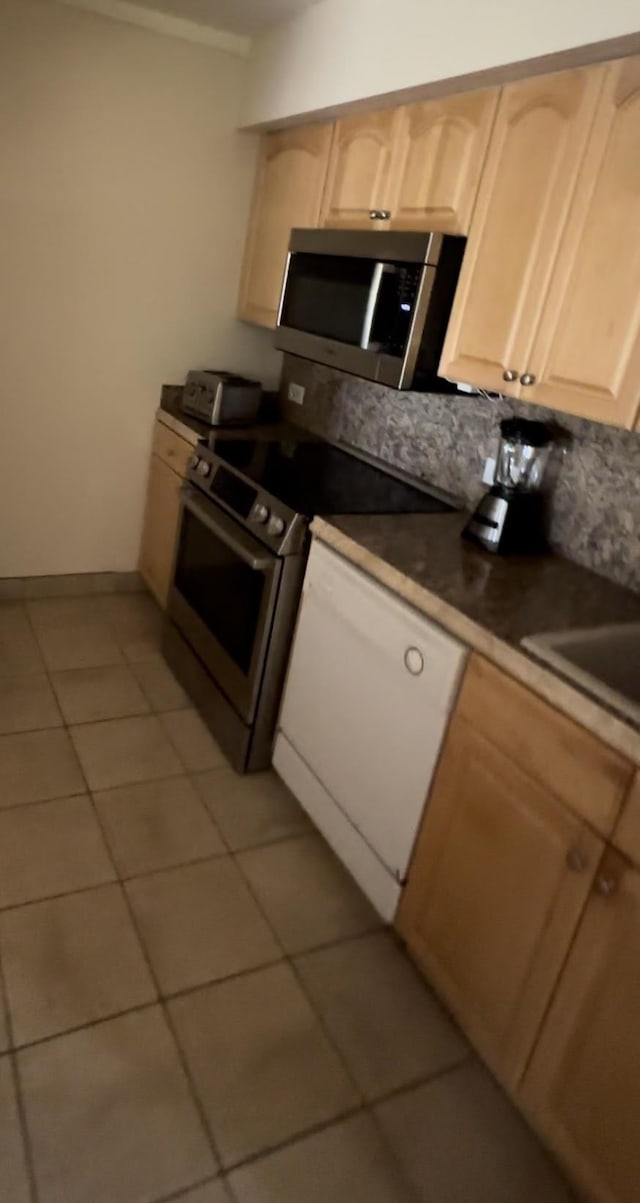 kitchen featuring dark countertops, appliances with stainless steel finishes, ornamental molding, light brown cabinetry, and light tile patterned flooring