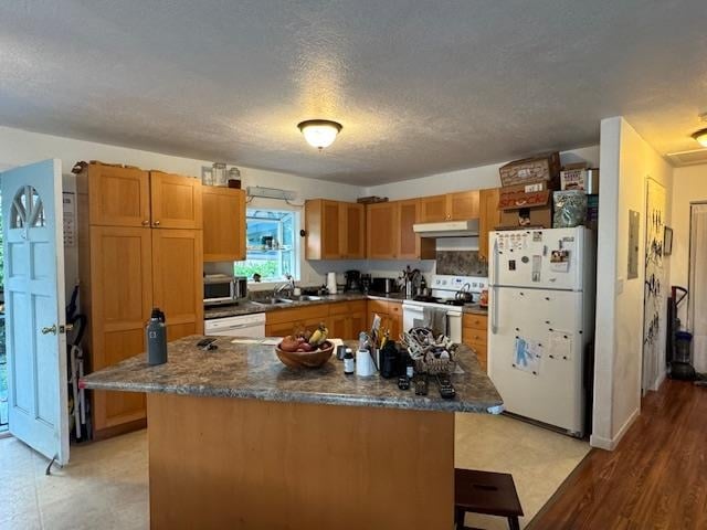 kitchen featuring white appliances, sink, light hardwood / wood-style floors, a kitchen island, and a breakfast bar area