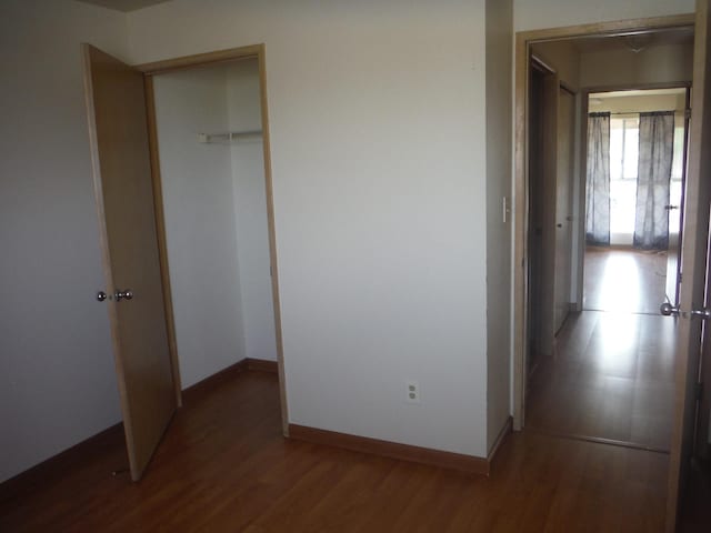 unfurnished bedroom with a closet, wood finished floors, and baseboards