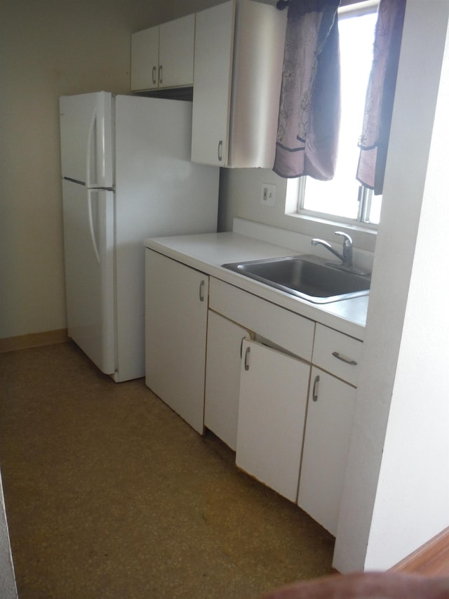 kitchen with light countertops, white cabinets, freestanding refrigerator, and a sink