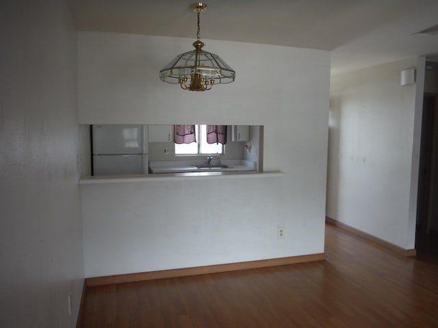 unfurnished dining area with a sink, an inviting chandelier, wood finished floors, and baseboards