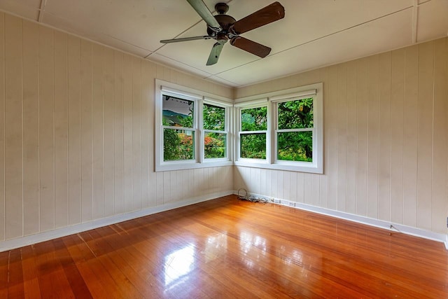 spare room with hardwood / wood-style flooring, ceiling fan, and wood walls