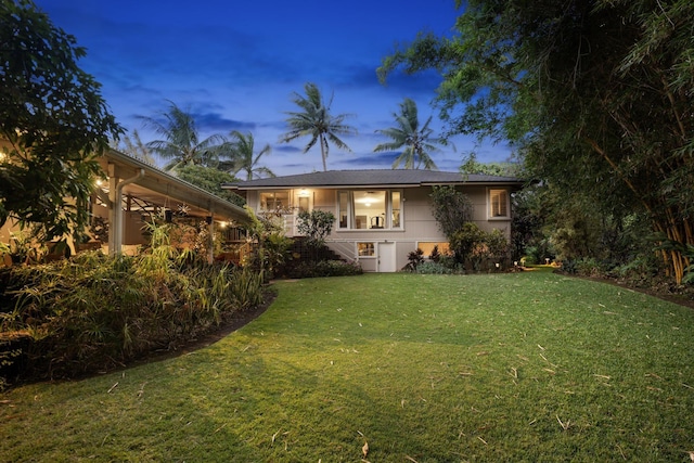 back house at dusk featuring a lawn