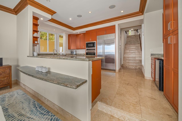 kitchen with light tile patterned floors, kitchen peninsula, beverage cooler, built in appliances, and stone counters