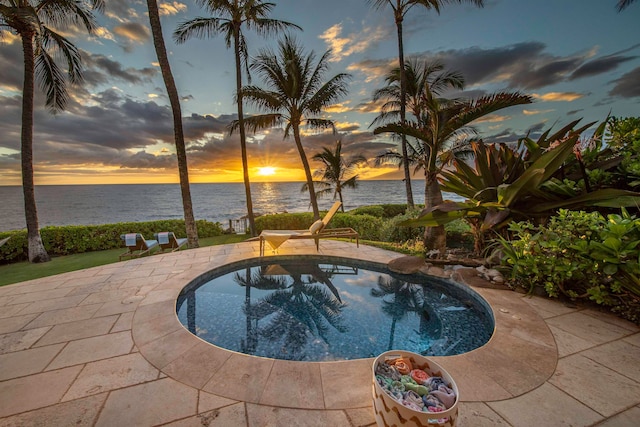 pool at dusk with a patio and a water view