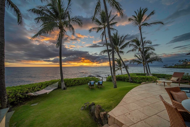 patio terrace at dusk with a water view and a yard