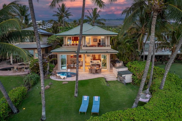 back house at dusk with a patio and a lawn