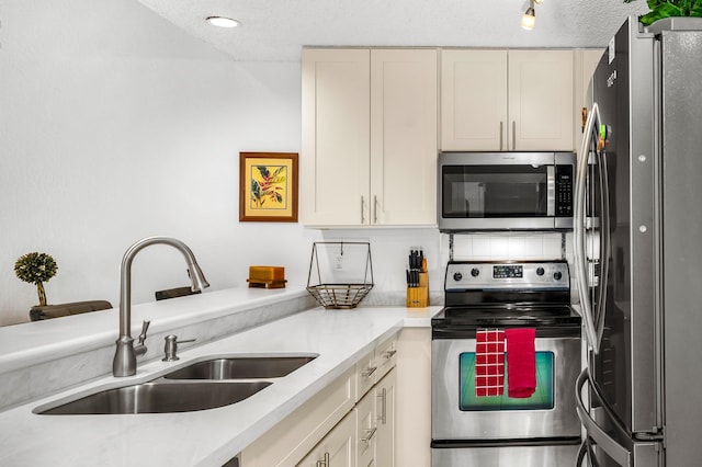 kitchen featuring a textured ceiling, stainless steel appliances, cream cabinetry, and sink