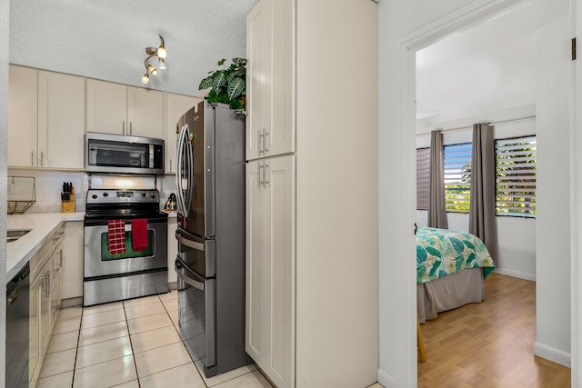 kitchen with appliances with stainless steel finishes, a textured ceiling, and light hardwood / wood-style floors