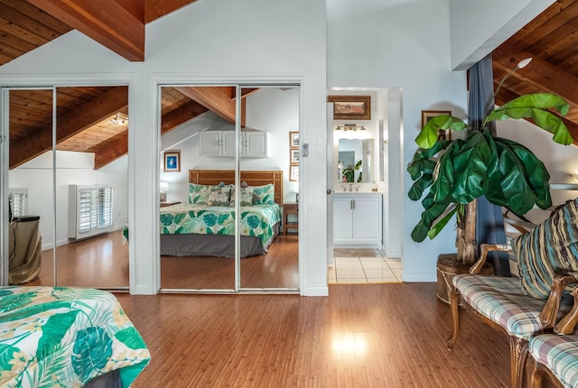 bedroom with vaulted ceiling with beams, light wood-type flooring, multiple closets, and wooden ceiling