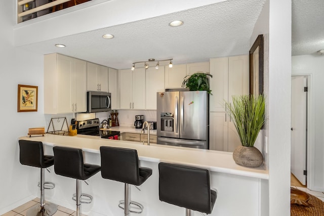 kitchen with a textured ceiling, kitchen peninsula, a breakfast bar area, and stainless steel appliances