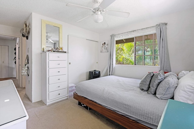 bedroom with a textured ceiling, ceiling fan, a closet, and light colored carpet