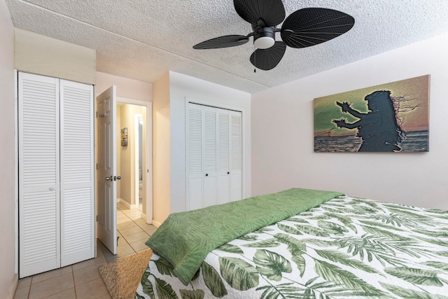 tiled bedroom featuring ceiling fan, two closets, and a textured ceiling