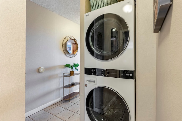 clothes washing area featuring light tile patterned flooring, stacked washer / drying machine, and a textured ceiling