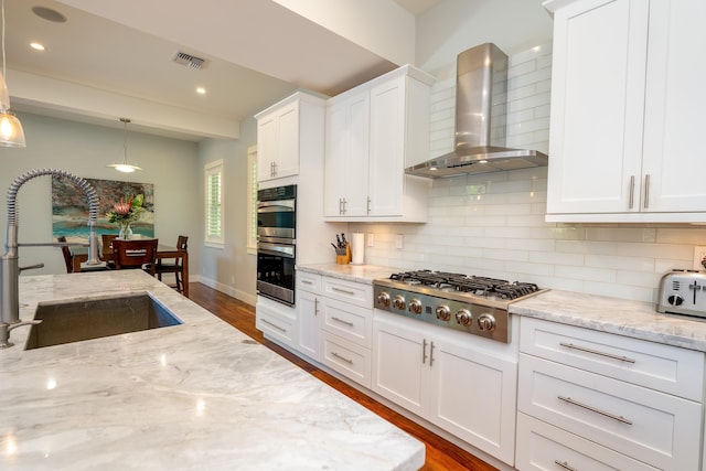 kitchen featuring visible vents, backsplash, appliances with stainless steel finishes, wall chimney exhaust hood, and a sink