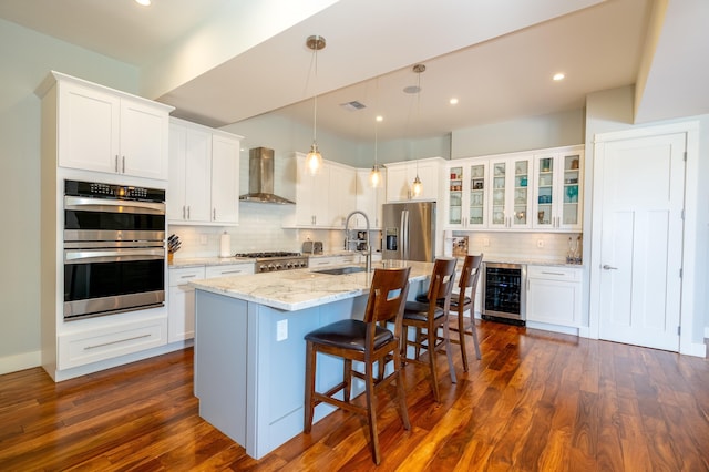 kitchen with a sink, dark wood-style floors, stainless steel appliances, wine cooler, and wall chimney range hood