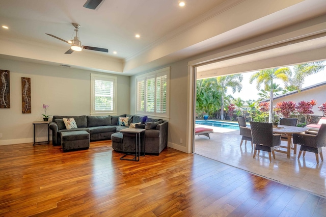 living room with wood finished floors, baseboards, a tray ceiling, ceiling fan, and ornamental molding