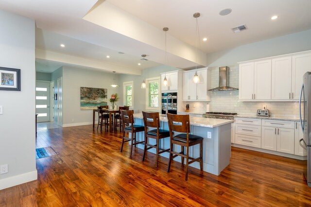 kitchen with visible vents, dark wood-type flooring, white cabinetry, wall chimney range hood, and decorative backsplash