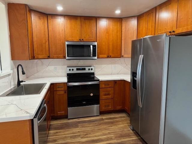 kitchen featuring sink, backsplash, stainless steel appliances, light stone counters, and dark hardwood / wood-style flooring