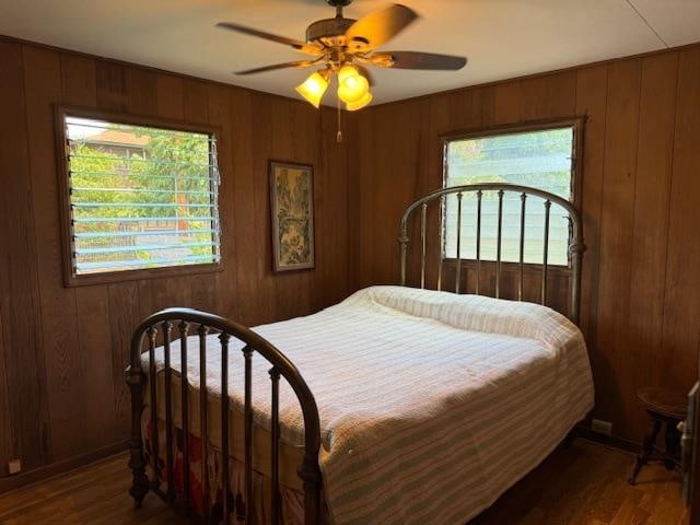 bedroom featuring wooden walls, ceiling fan, and dark wood-type flooring