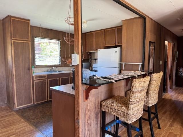 kitchen featuring a kitchen bar, wooden walls, dark wood-type flooring, sink, and white fridge