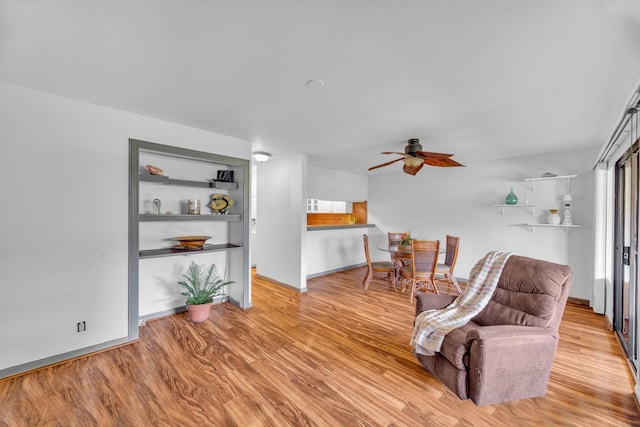 living area featuring baseboards, ceiling fan, and light wood-style flooring