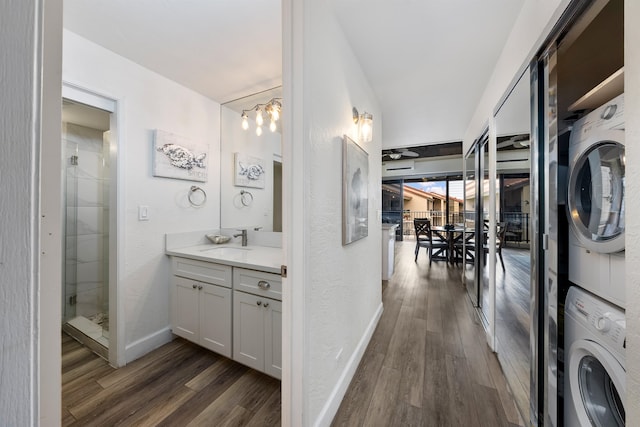 bathroom featuring stacked washing maching and dryer, a tile shower, large vanity, and wood-type flooring