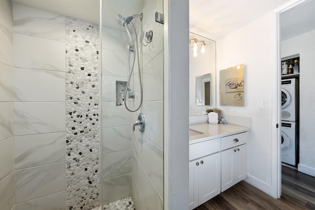 bathroom featuring a tile shower, vanity with extensive cabinet space, stacked washer / dryer, and wood-type flooring