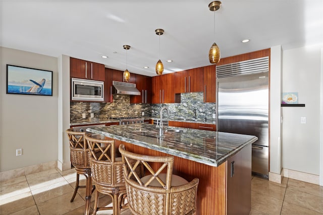 kitchen featuring decorative backsplash, light tile patterned flooring, under cabinet range hood, a sink, and built in appliances