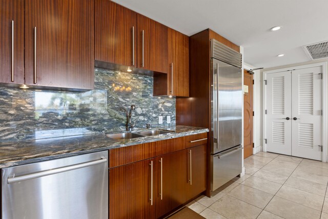 kitchen with dark stone counters, tasteful backsplash, light tile patterned floors, sink, and appliances with stainless steel finishes